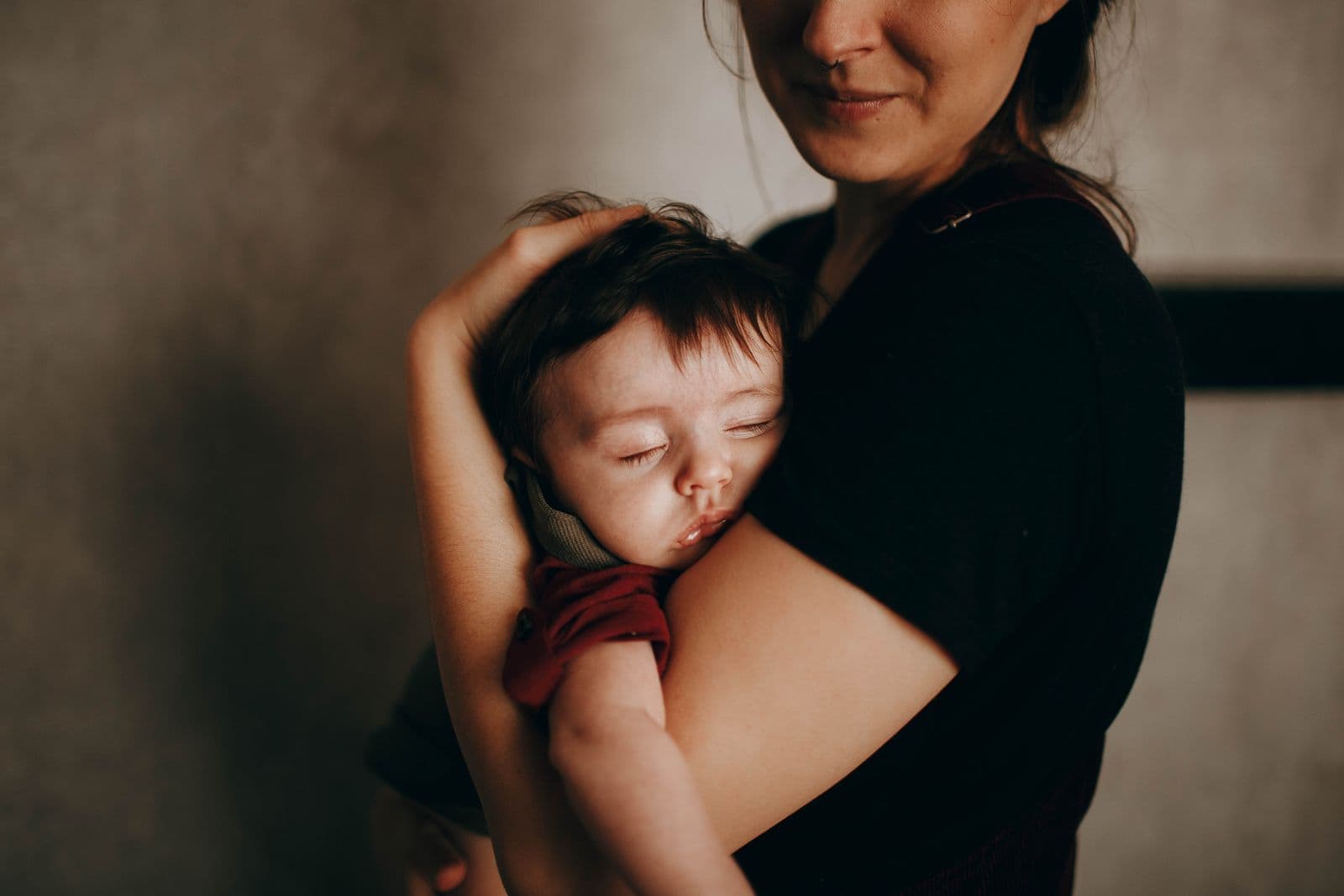 A mother cradles her sleepy baby against a dark wall.